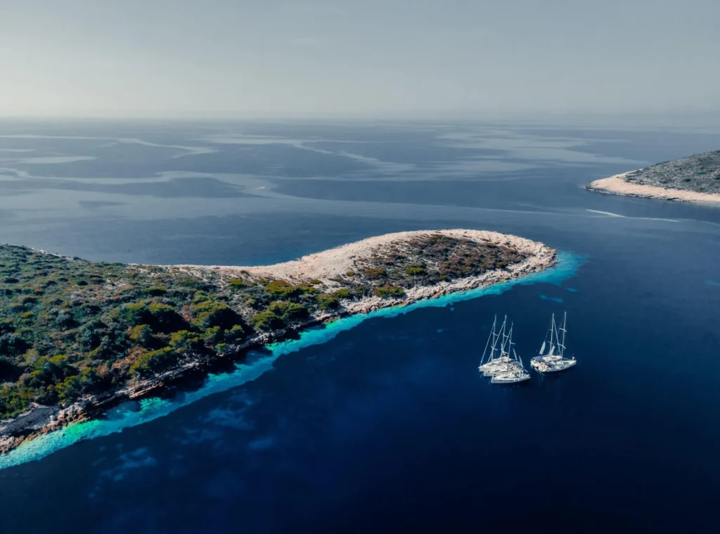 Sailing yachts cruising through clear Adriatic waters along a coastal island