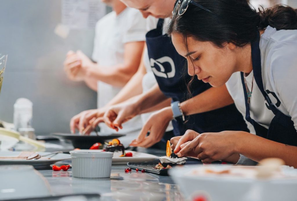 Culinary Academy students plating dishes during a professional cooking session.