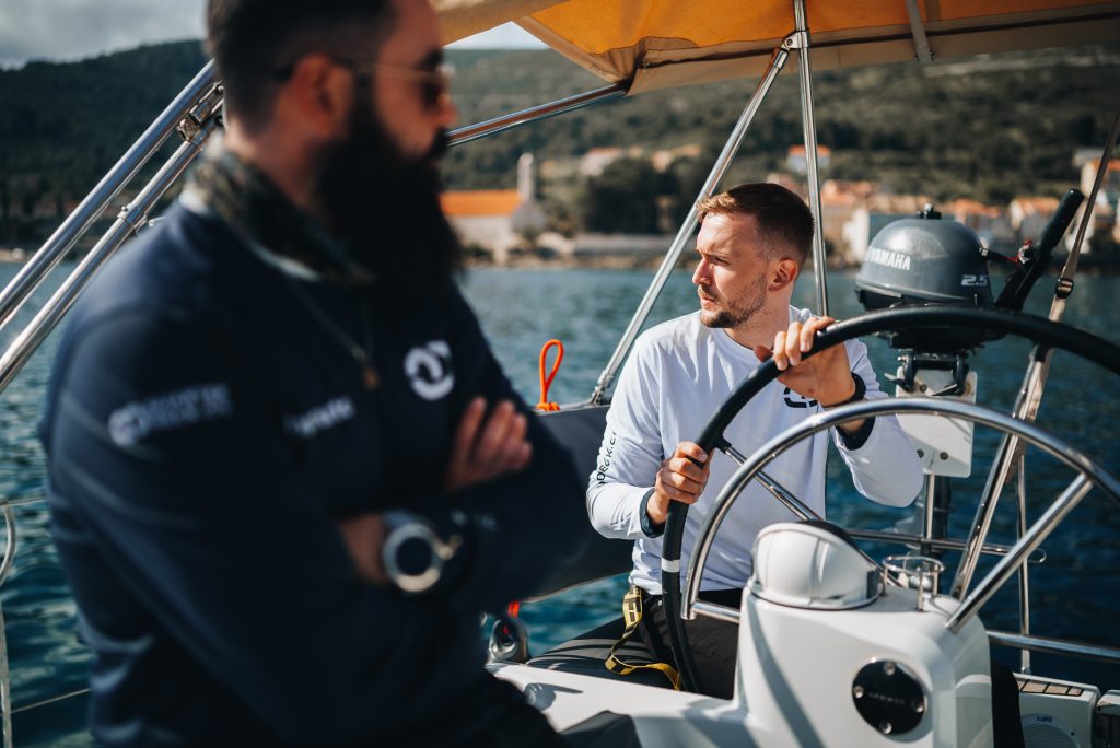 A beginner yacht crew member steering a sailboat under guidance, illustrating how to work on yachts
