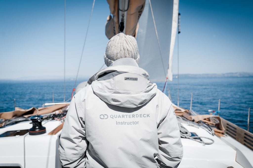 Quarterdeck instructor standing at the bow of a sailboat looking out toward open water.