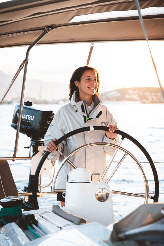 Female Skipper Academy student smiling at the helm while practicing yacht maneuvering and steering techniques.