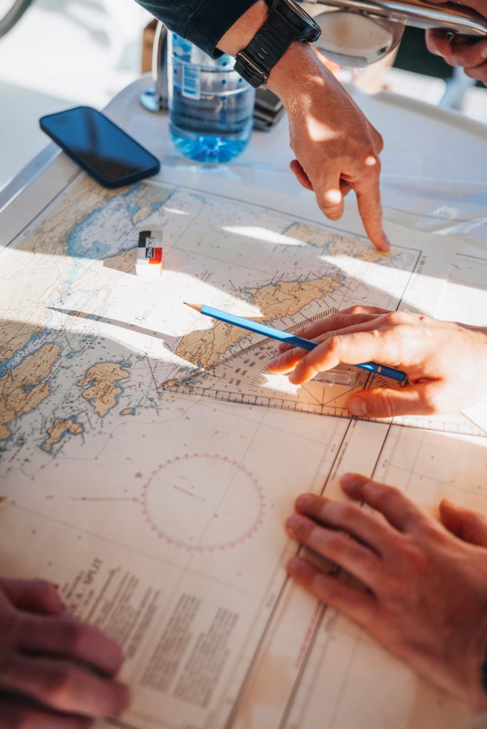 Skipper Academy students using a pencil and ruler to plot a passage plan on a nautical chart during navigation training.